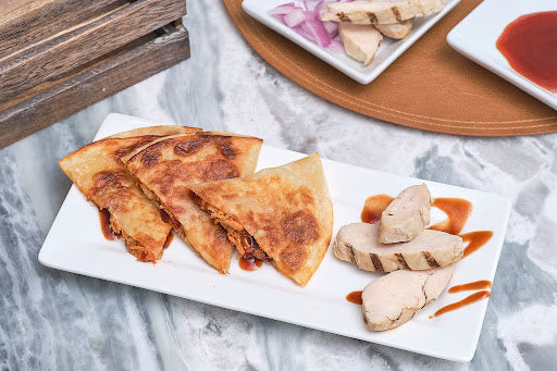Rise & Puff Chipotle Chicken Quesadilla served on a plate with dipping sauce and sliced grilled chicken on the side.