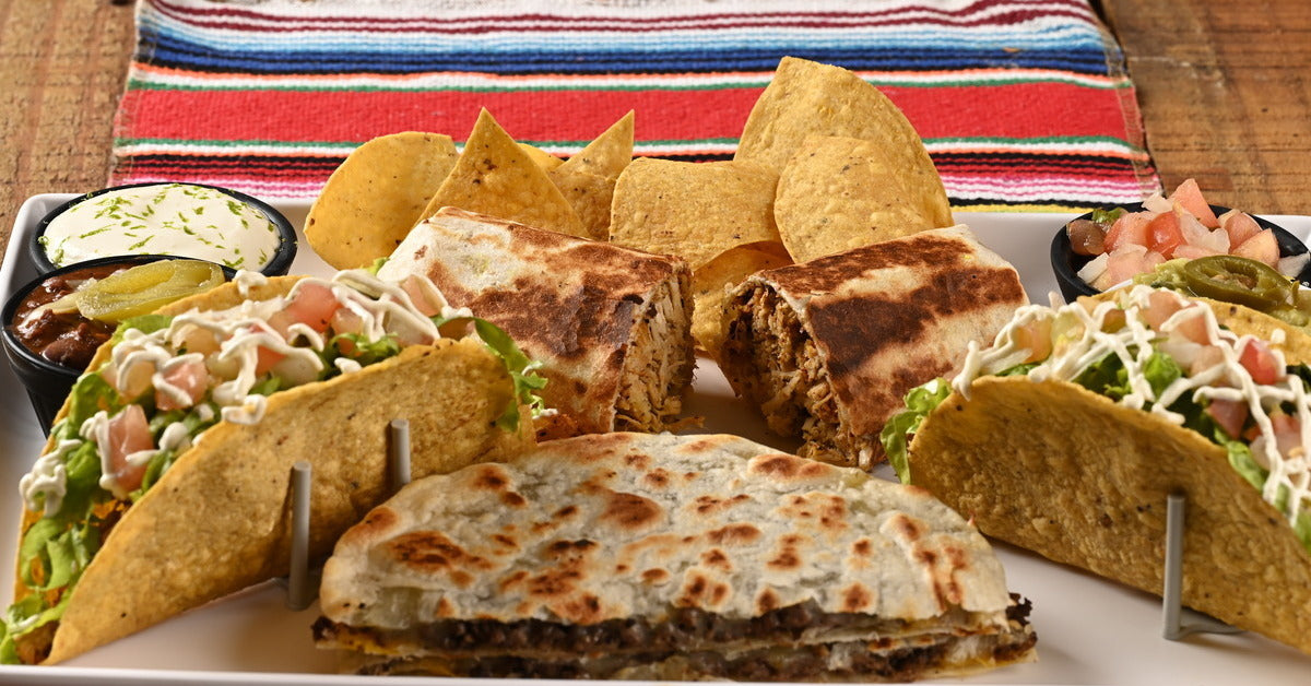 A spread of Mexican cuisine, including tacos, quesadillas, burritos, and tortilla chips for nachos served on a plate.