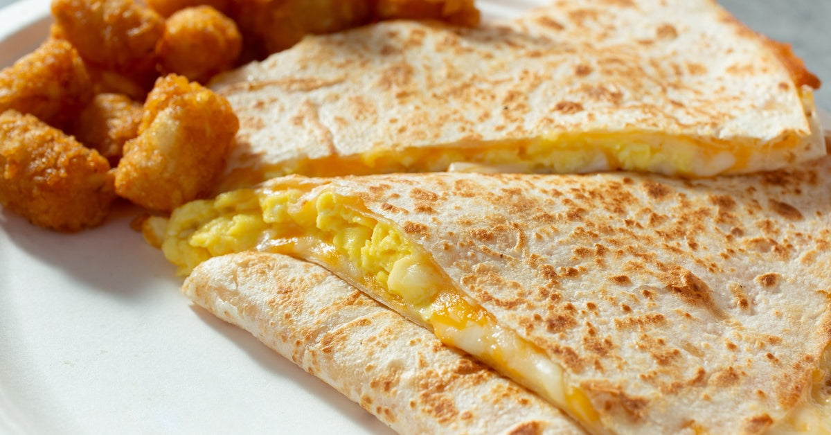 A plate of breakfast quesadillas filled with eggs, cheese, and tater tots on a rustic wooden table.