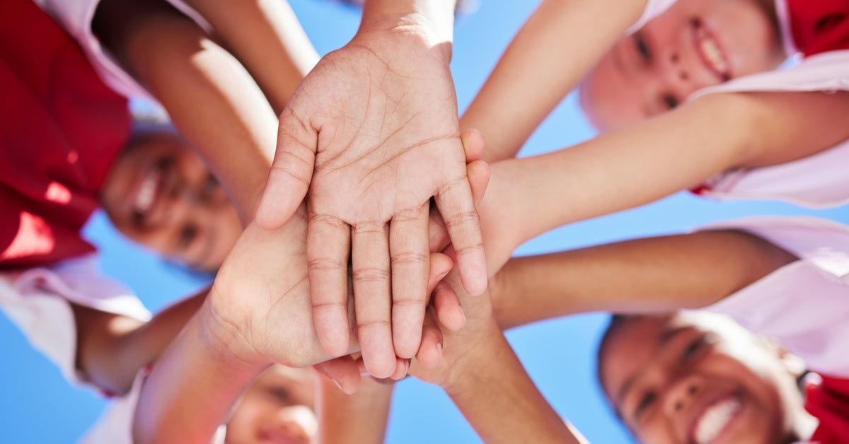 A team of young soccer players is wearing matching jerseys. In a huddle, they place their hands in the middle while smiling.