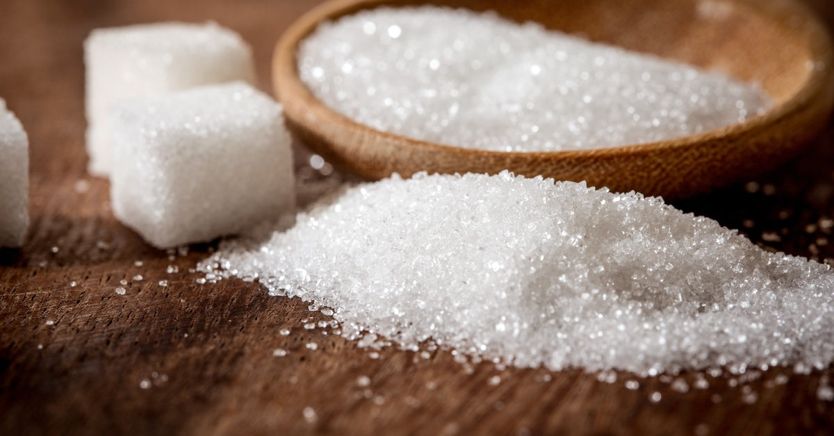 Sugar cubes and sugar granules lie on a round wooden bowl atop a table, showing their multiple shapes and textures.