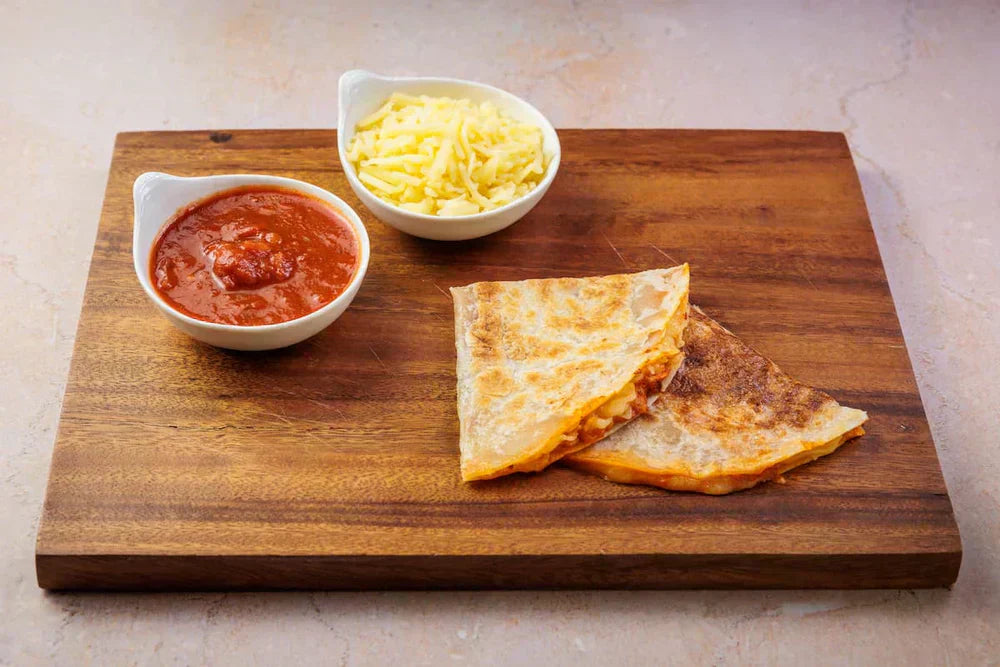 Rise & Puff pizza quesadilla sliced and served on a wooden board with melted cheese and crisp tortilla edges.