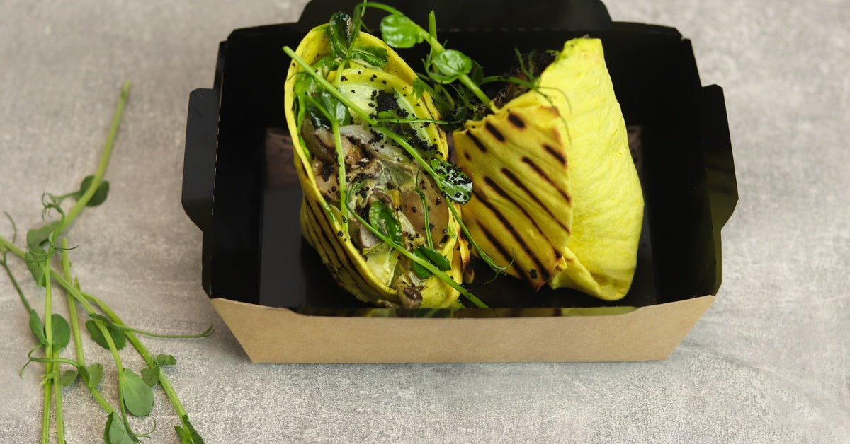 A black and brown paperboard box holding two quesadillas containing chicken, mushrooms, and a leafy garnish.