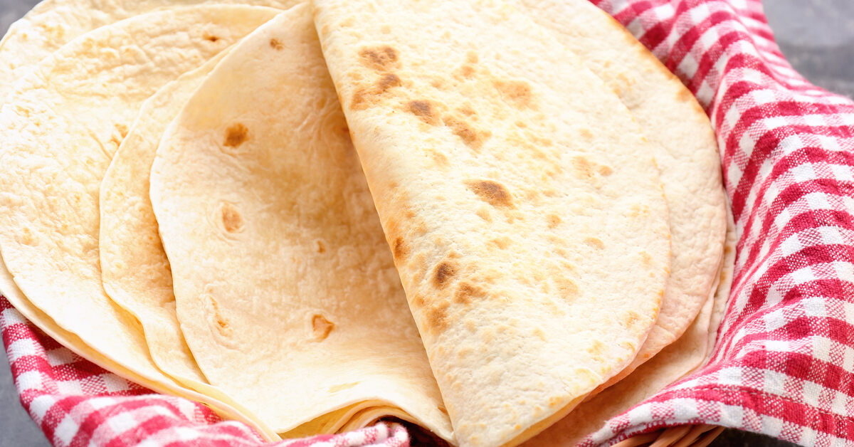 A wicker basket covered in a red and white striped cloth. White flour tortillas sit inside the cloth.