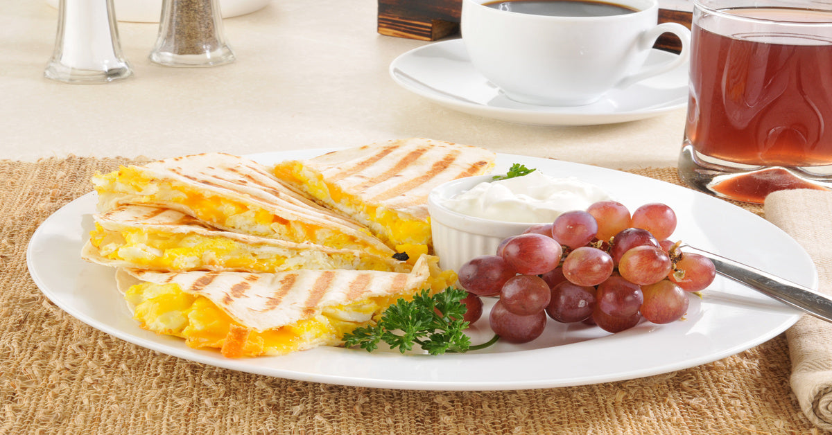 A plate of quesadillas filled with eggs and cheese with a side of red grapes and a bowl of sour cream.