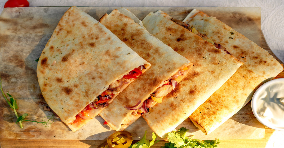 A wooden platter of quesadillas filled with meat and peppers with a slice of jalapeños and leafy garnish on the side.