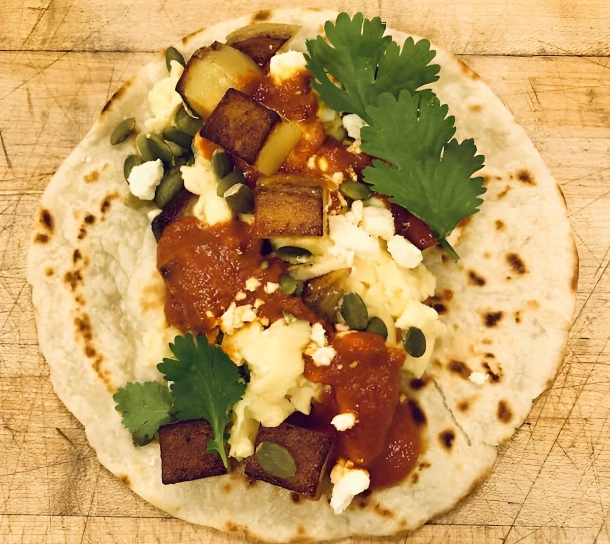 Rise & Puff tortilla topped with roasted vegetables, creamy cheese, fresh salsa, and cilantro on a wooden board.