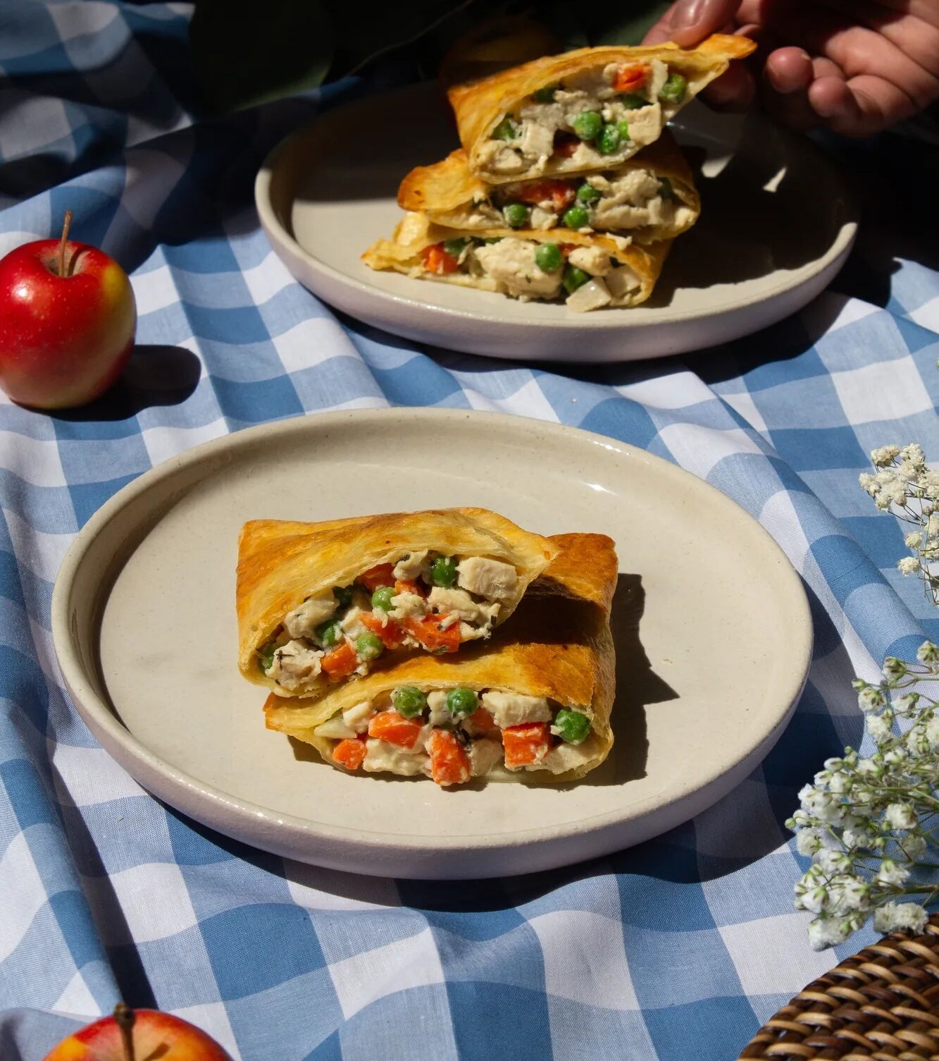 Chicken Pot pie on a white plate on a picnic table with apples and flowers