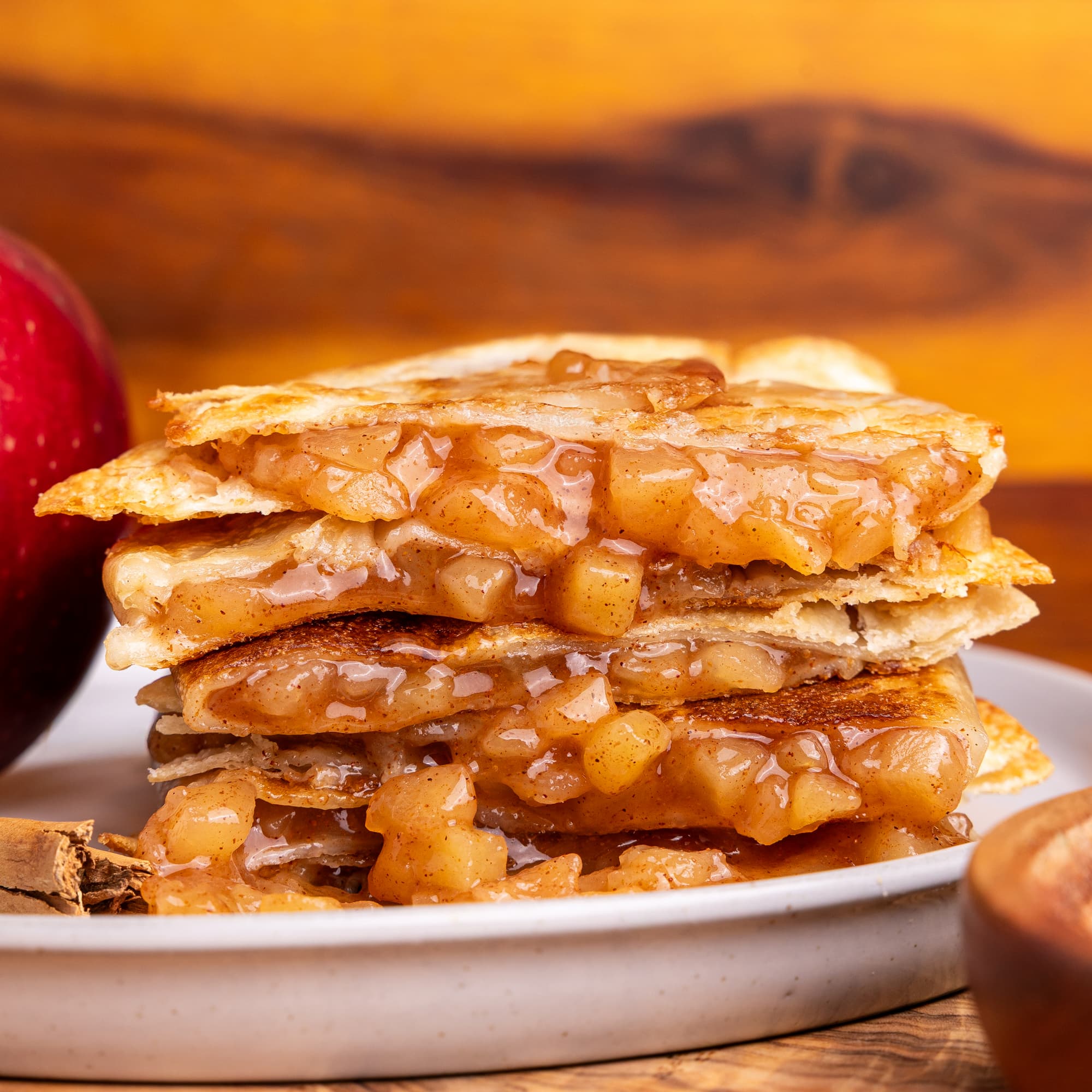 a stack of flaky apple dessert layers topped with powdered sugar, served with fresh apples and cinnamon sticks.