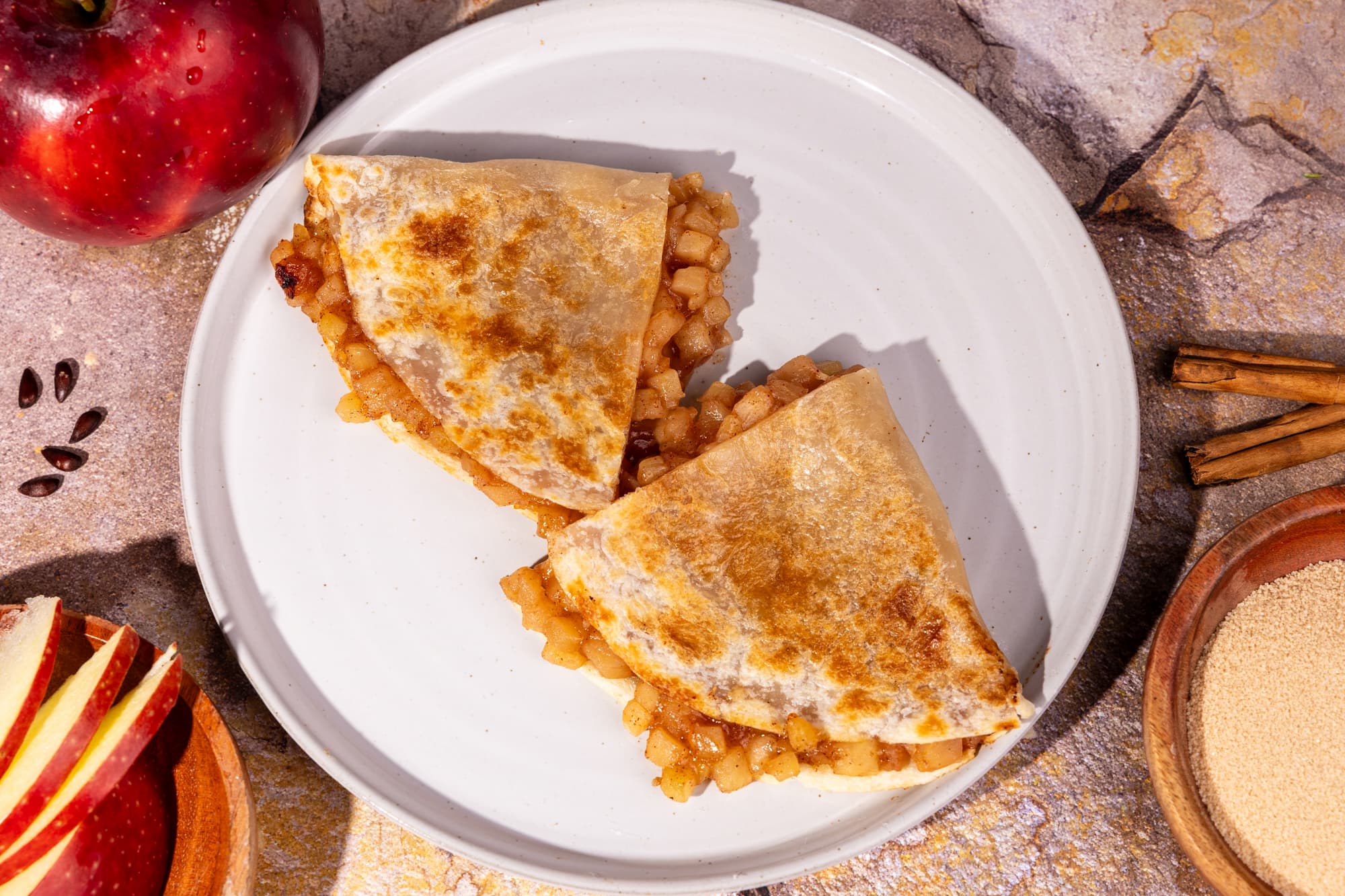 Rise & Puff healthy apple pie on a white plate with the ingredients around it showing an apple and cinnamon.
