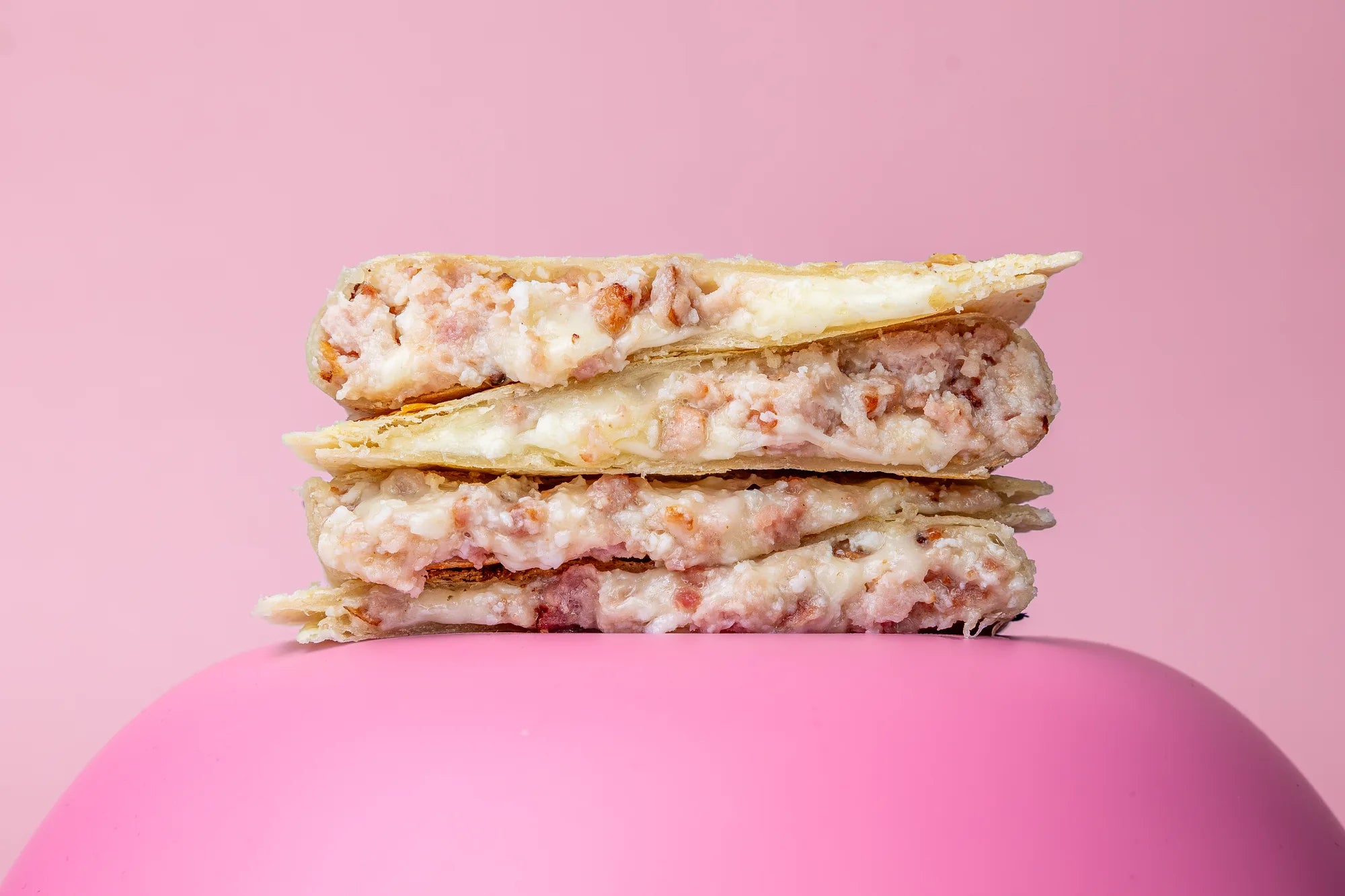 Stack of Bacon Egg & Cheese quesadillas on a pink platform with a pink background