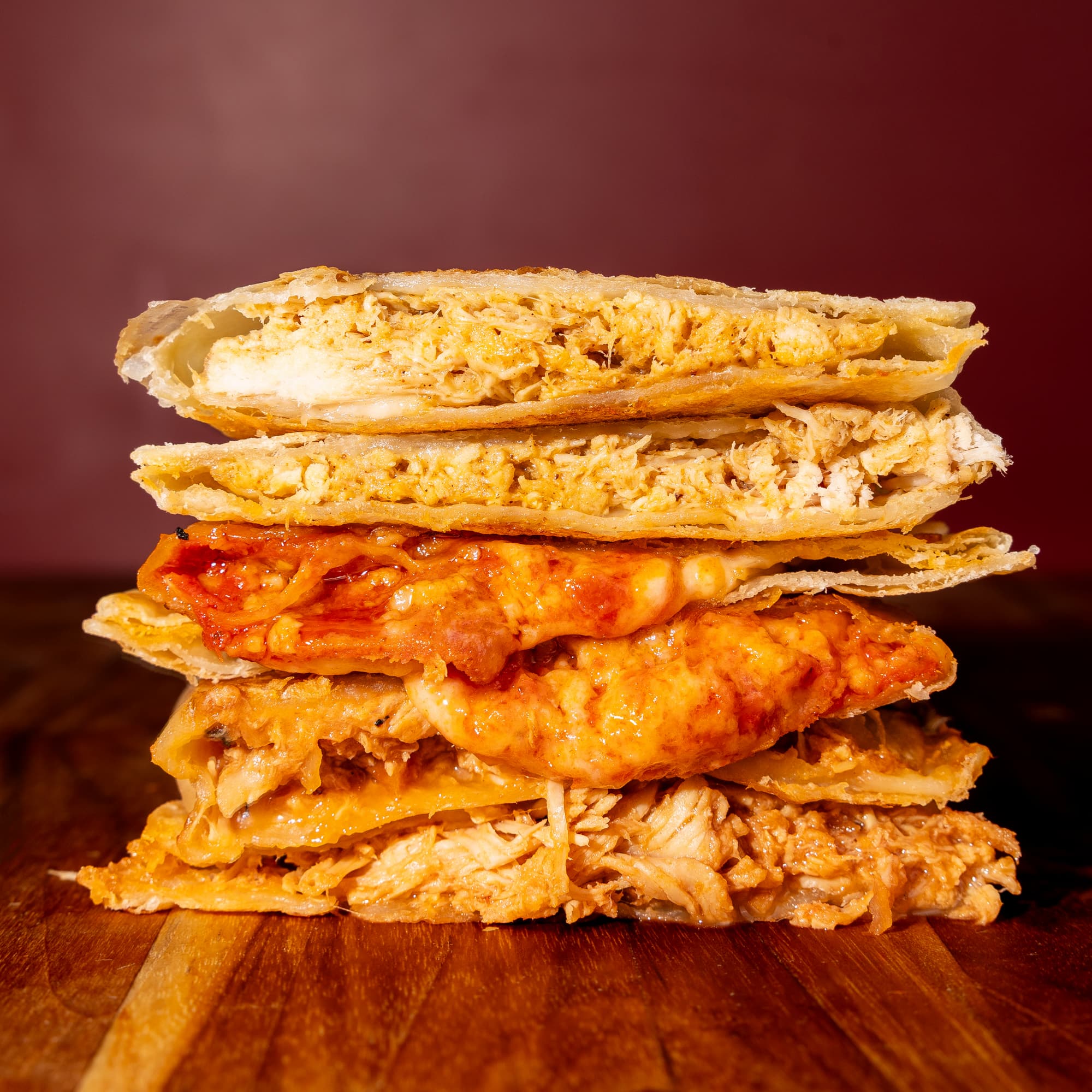 A close-up of a stacked Rise & Puff quesadillas on a wooden board against a dark reddish-brown background.