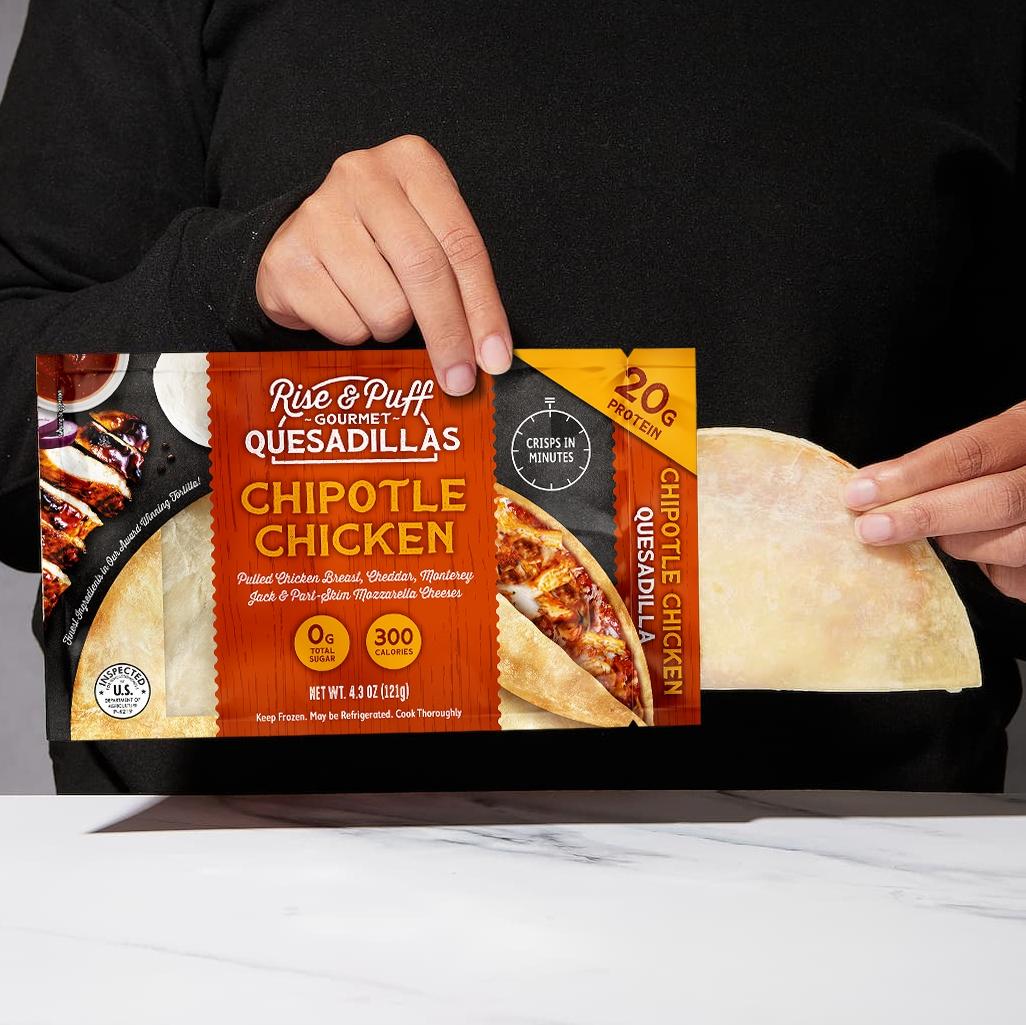 Person holding a package of Rise & Puff Gourmet Quesadillas Chipotle Chicken flavor on a white surface.