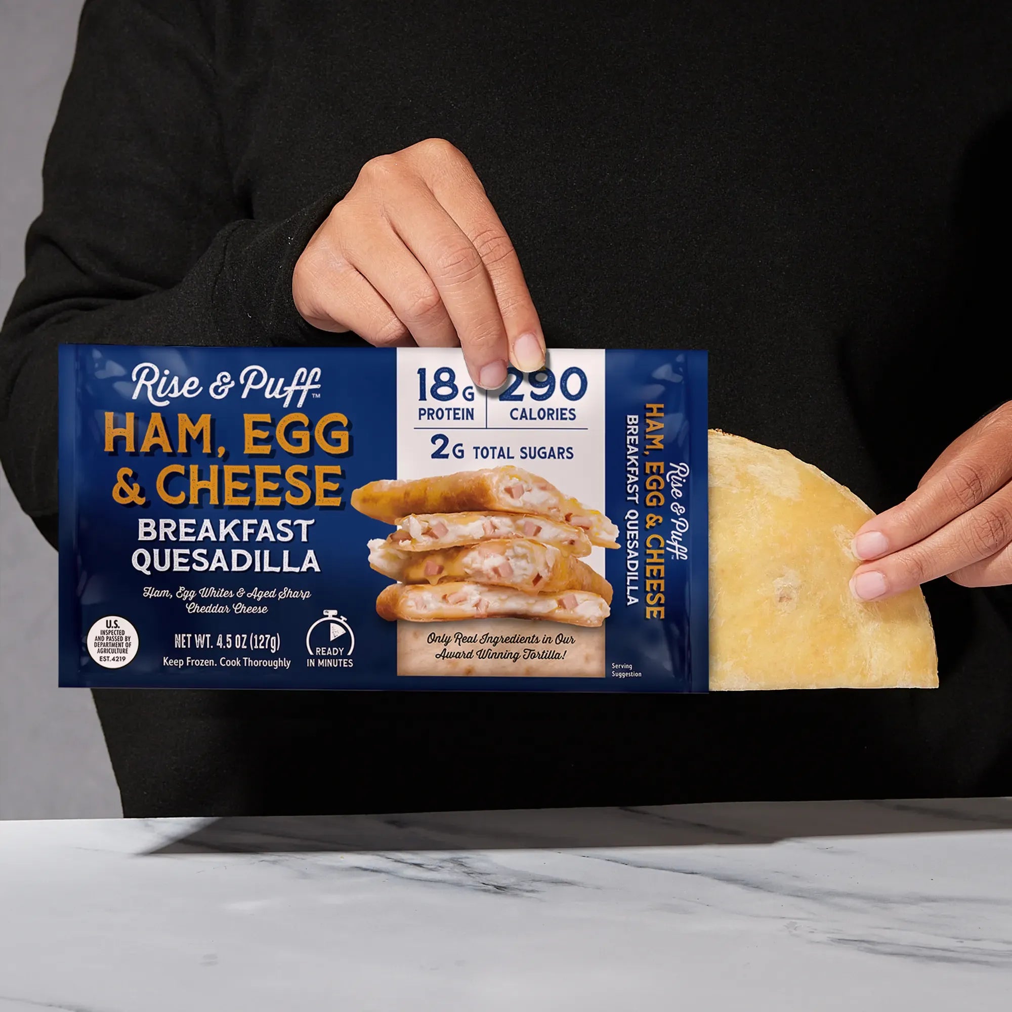Rise & Puff Ham, Egg & Cheese Breakfast Quesadilla shown coming out of its frozen retail packaging