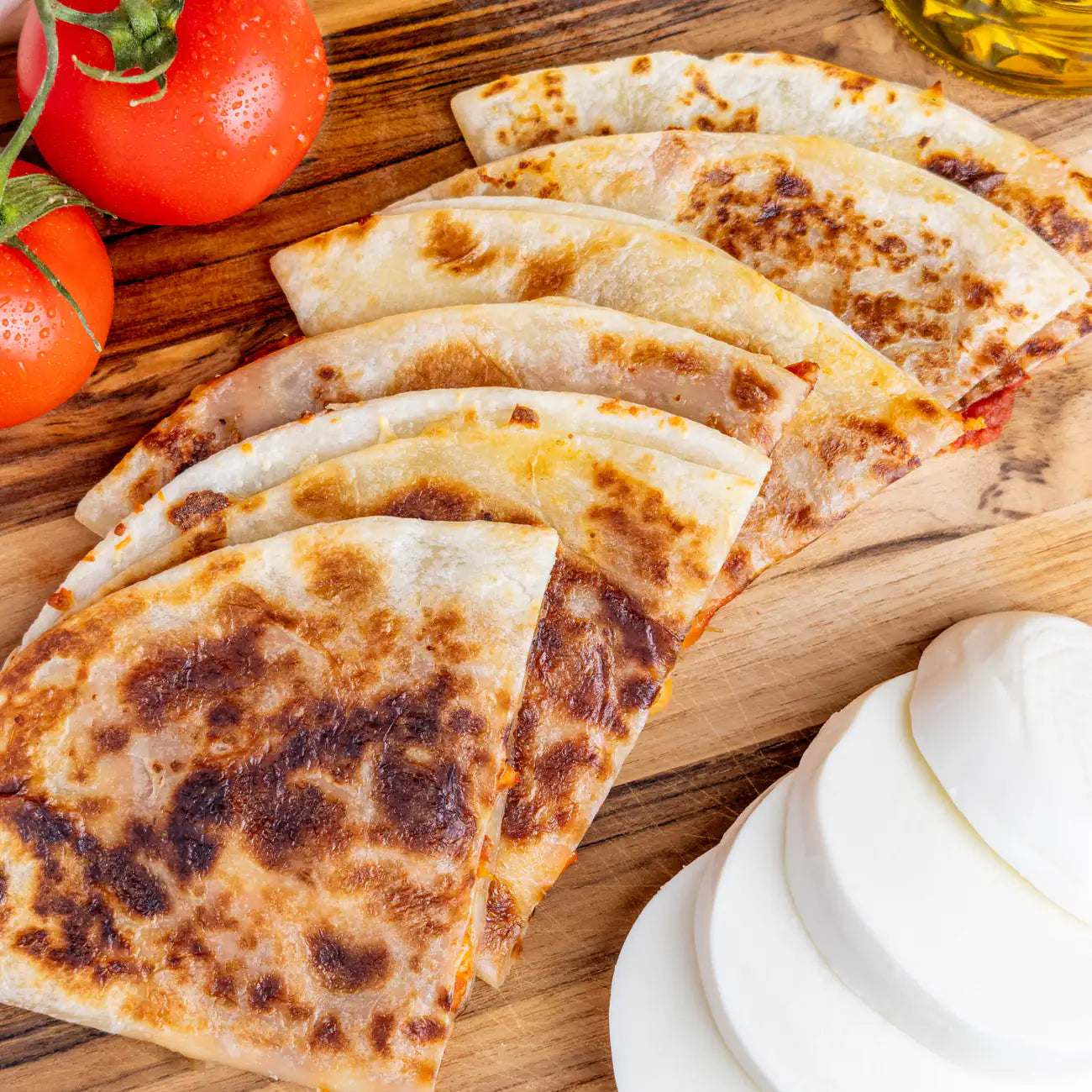 Margherita Pizza Quesadilla on cutting board with tomatoes and mozzarella cheese