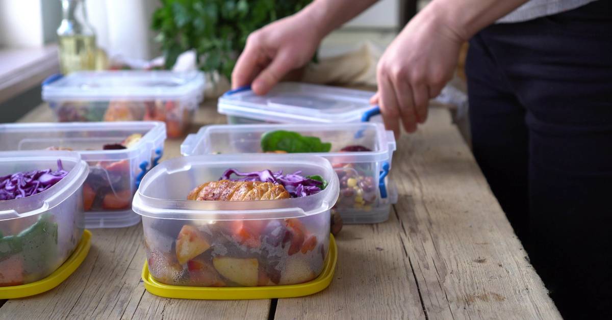 Plastic containers filled with the same food options line a table as someone places the lids for storage.