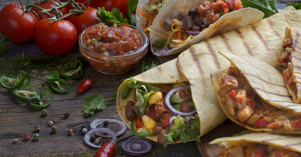 A spread of quesadillas and burritos on a wooden surface, each containing a variety of meats and vegetables.