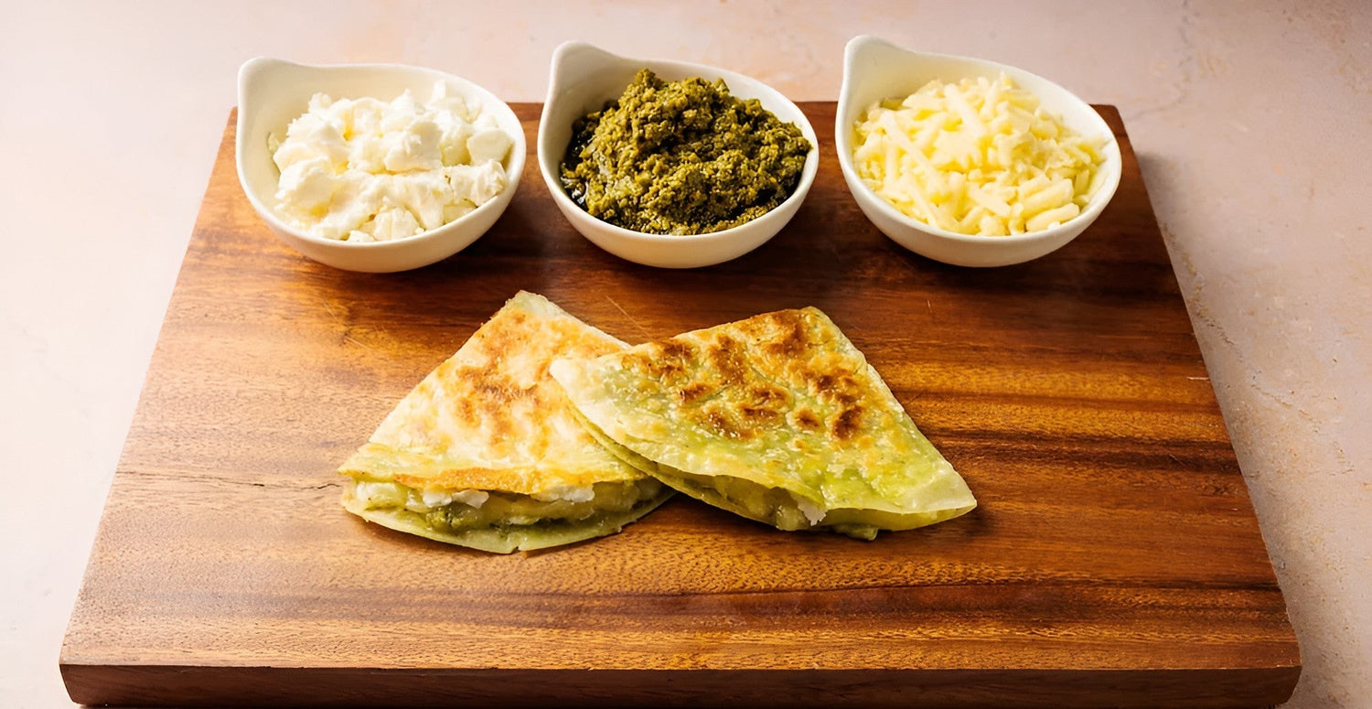 Rise and Puff pesto quesadillas on a wooden board with bowls of cheese and pesto ingredients.