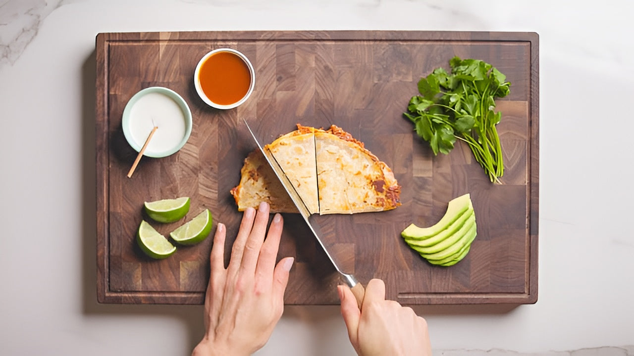 Rise and Puff quesadilla being sliced on a wooden board with avocado, lime, cilantro, and dipping sauces.