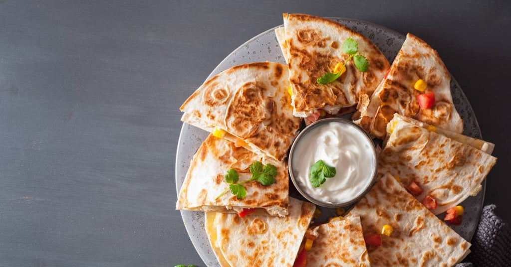 A plate with sour cream in the center holds a circle of grilled tortillas filled with cheese, tomatoes, and chicken.