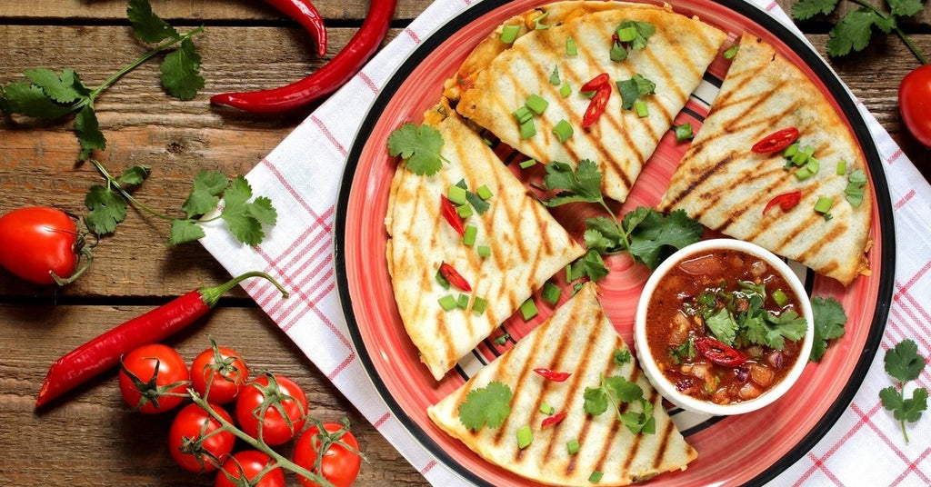 A plate of four quesadillas topped with garnishes, peppers, and small vegetables in a semicircle around a small bowl of salsa.