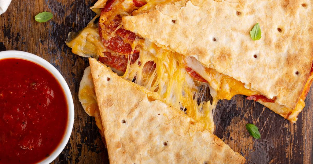 A pizza quesadilla cut into tringles is pulled apart to reveal strands of cheese and slices of pepperoni.