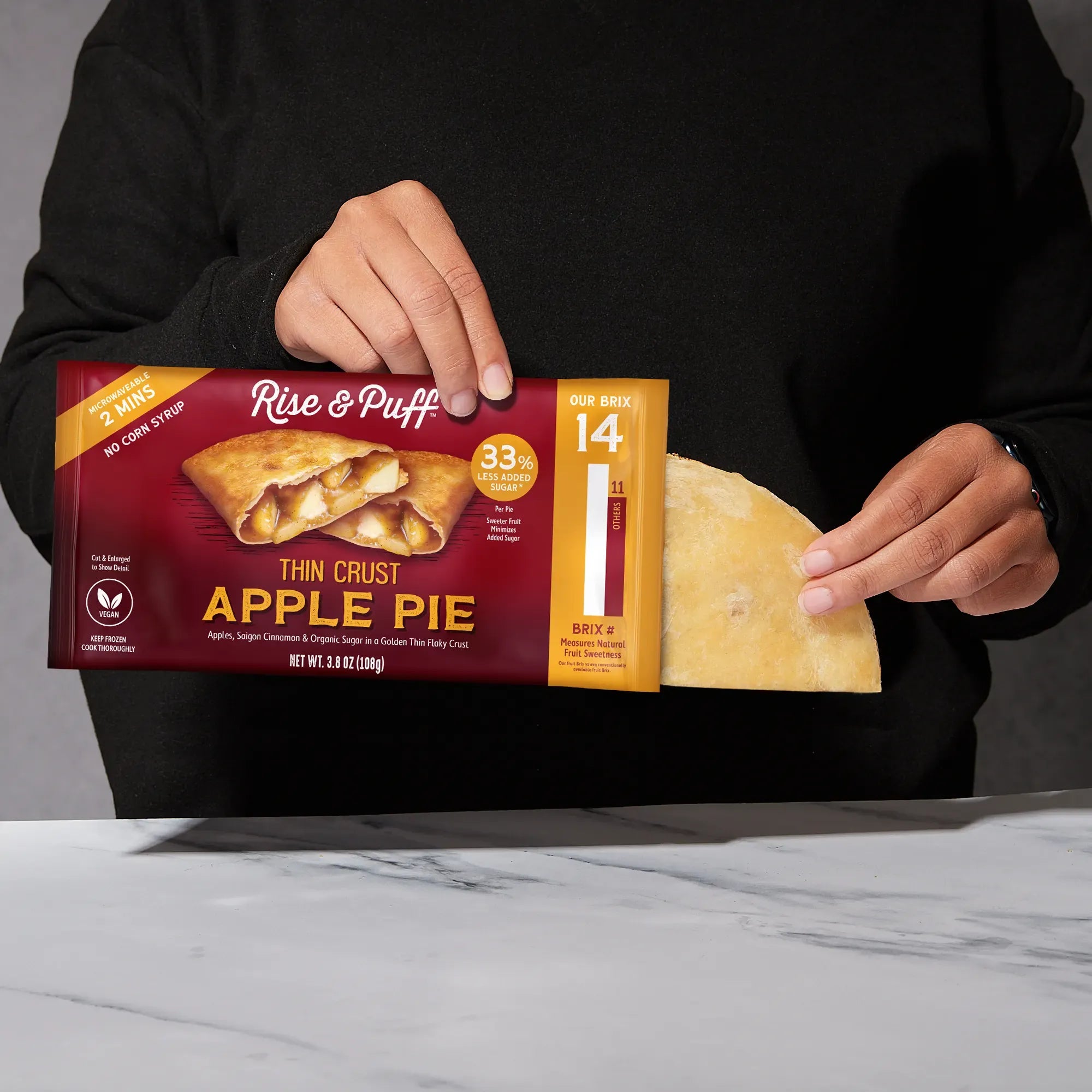Rise & Puff Thin Crust Apple Pie sliding out of its package — frozen handheld apple pie with golden thin flaky crust, Saigon cinnamon and organic sugar, net wt 3.8 oz