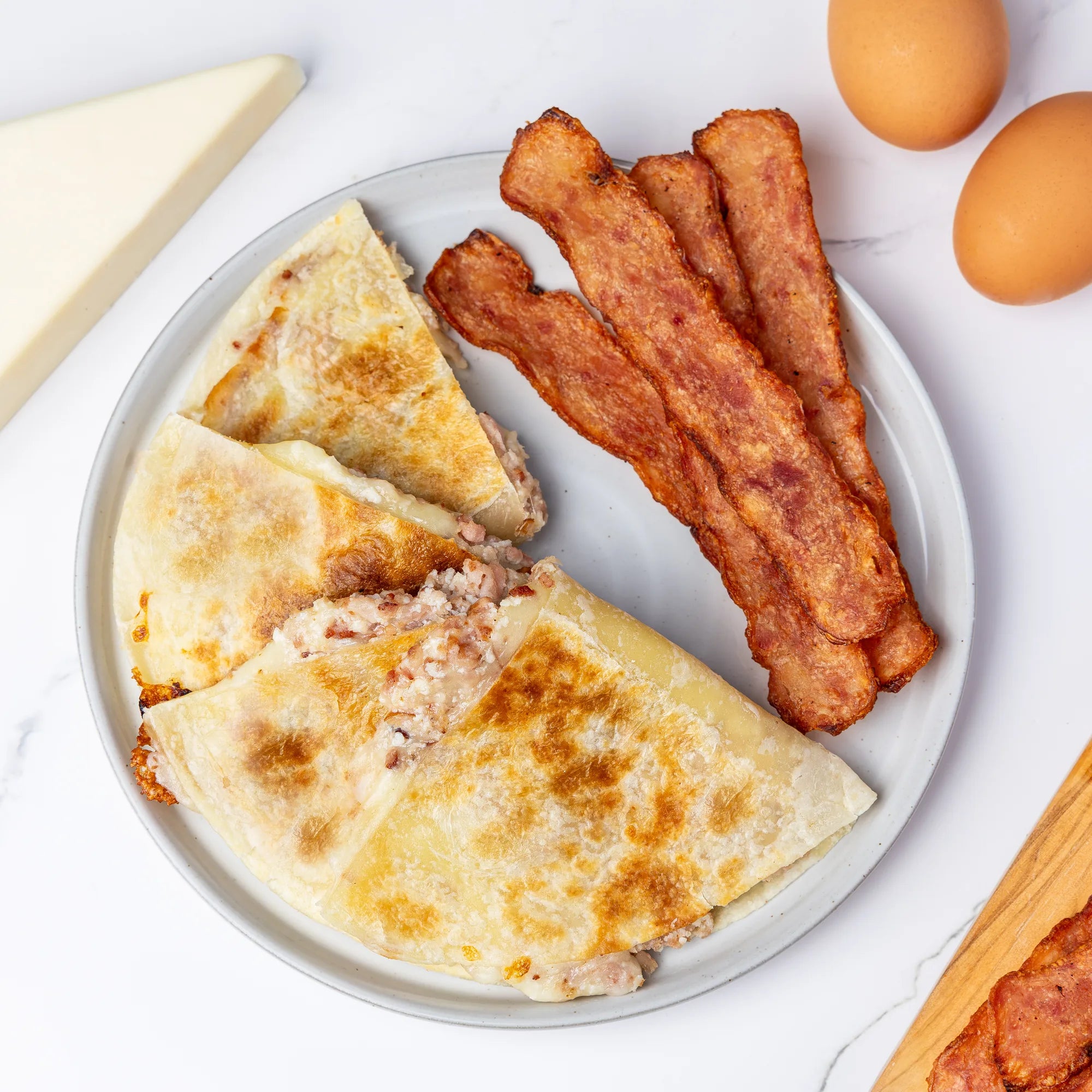 Plate of quesadillas with bacon and eggs on a white surface