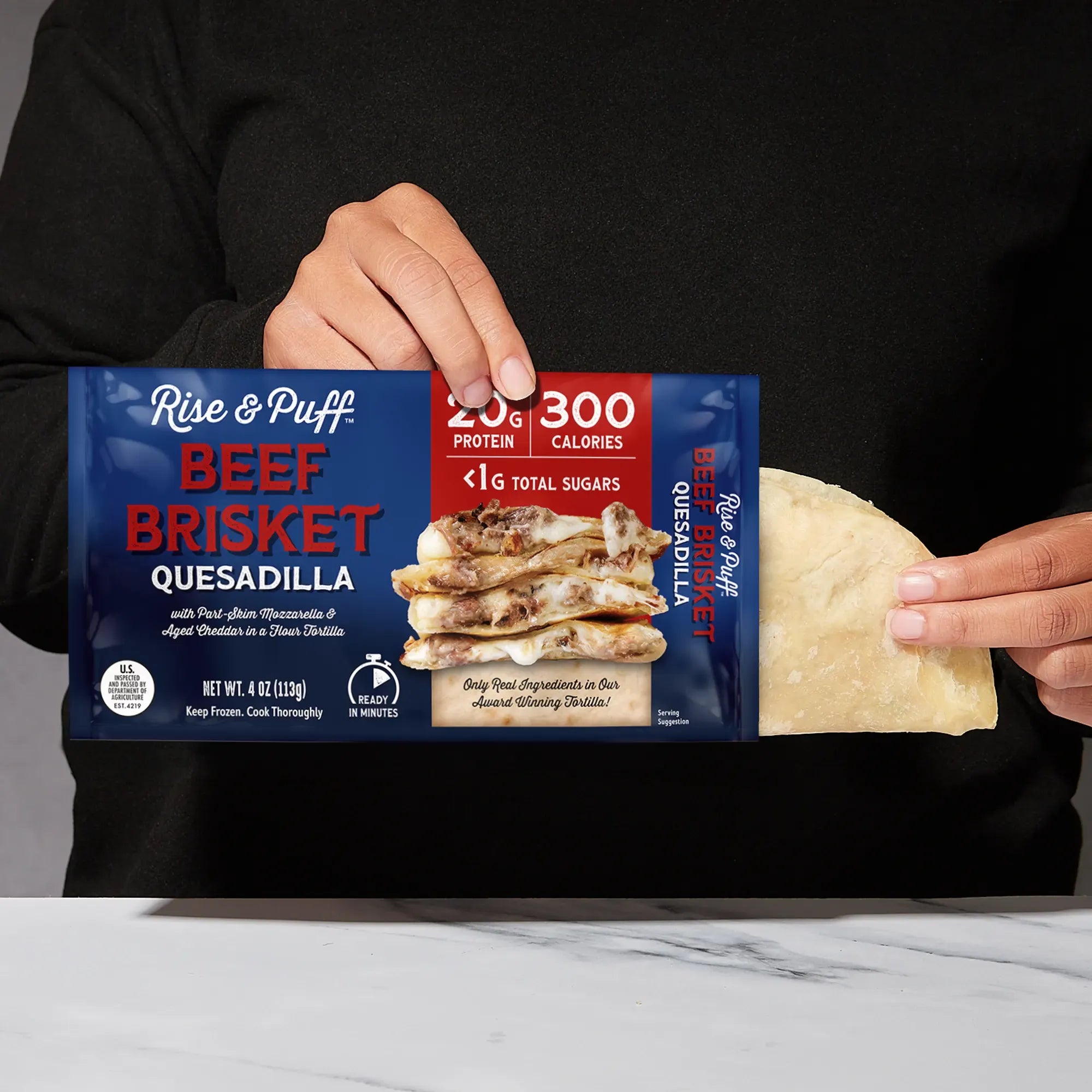 Rise & Puff Beef Brisket Quesadilla shown coming out of its frozen retail packaging