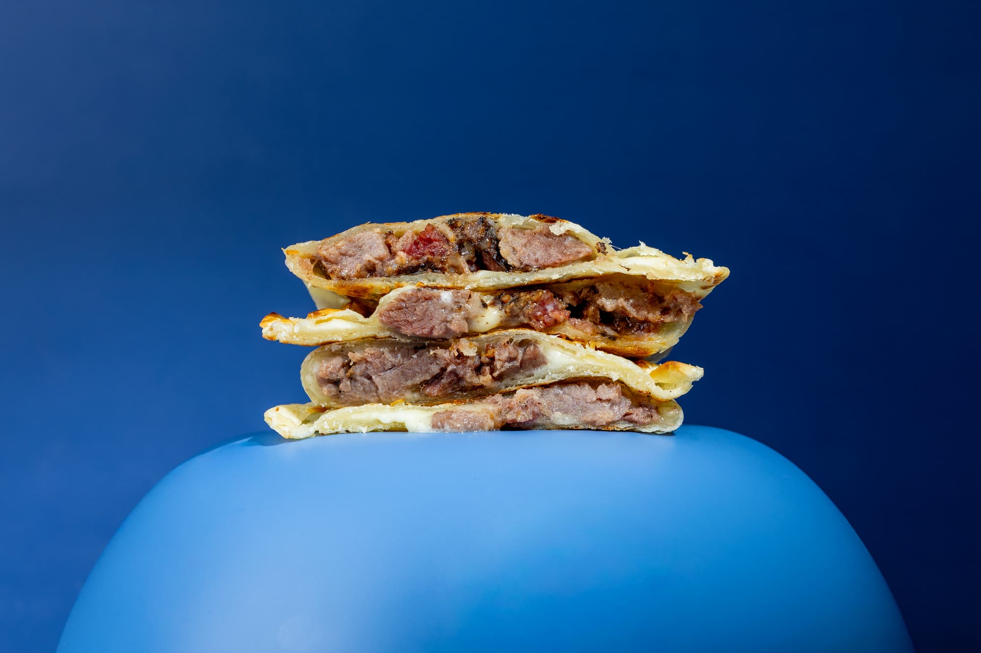 Stack of meat-filled pastries on a blue pedestal with a blue background