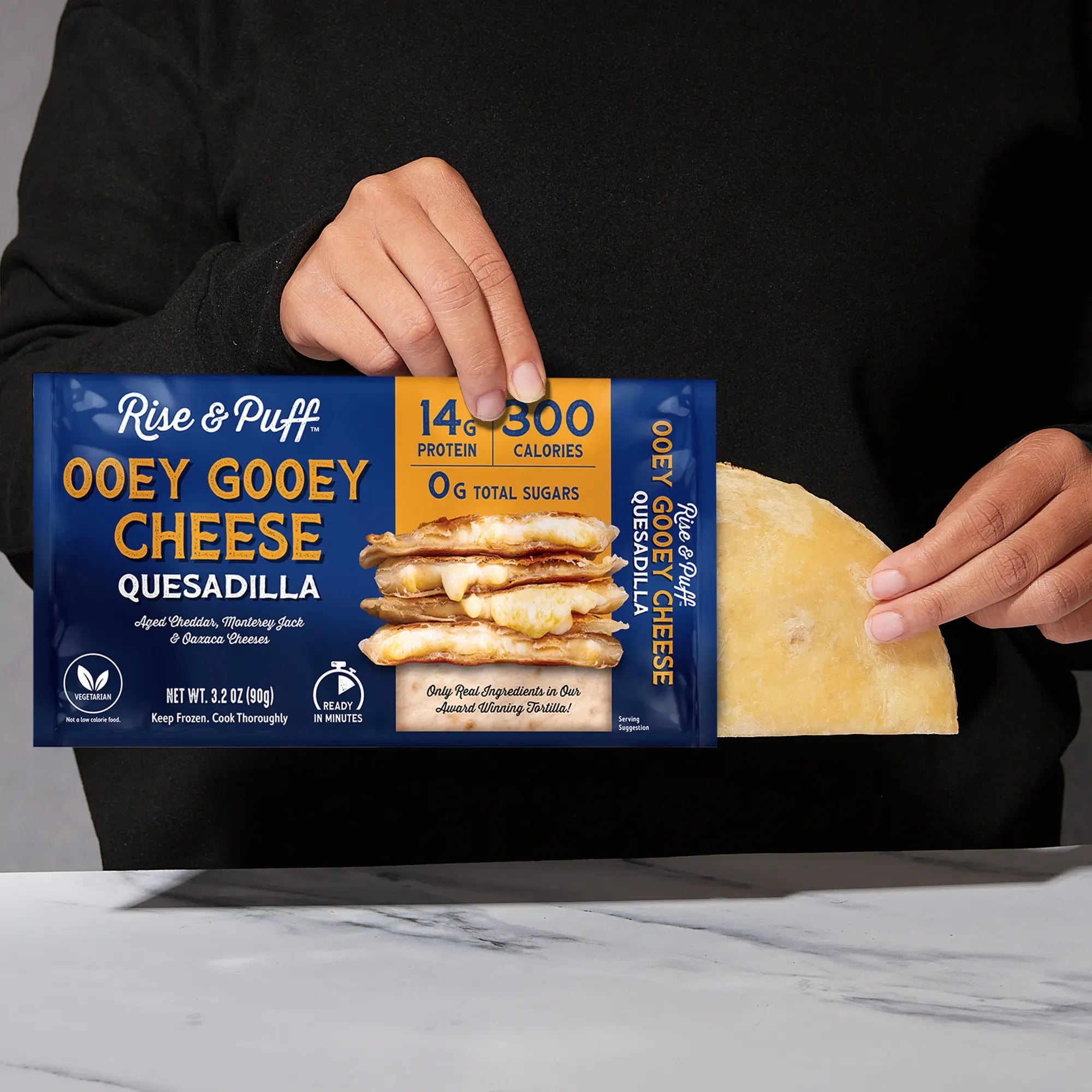 Rise & Puff Ooey Gooey Cheese Quesadilla shown coming out of its frozen retail packaging