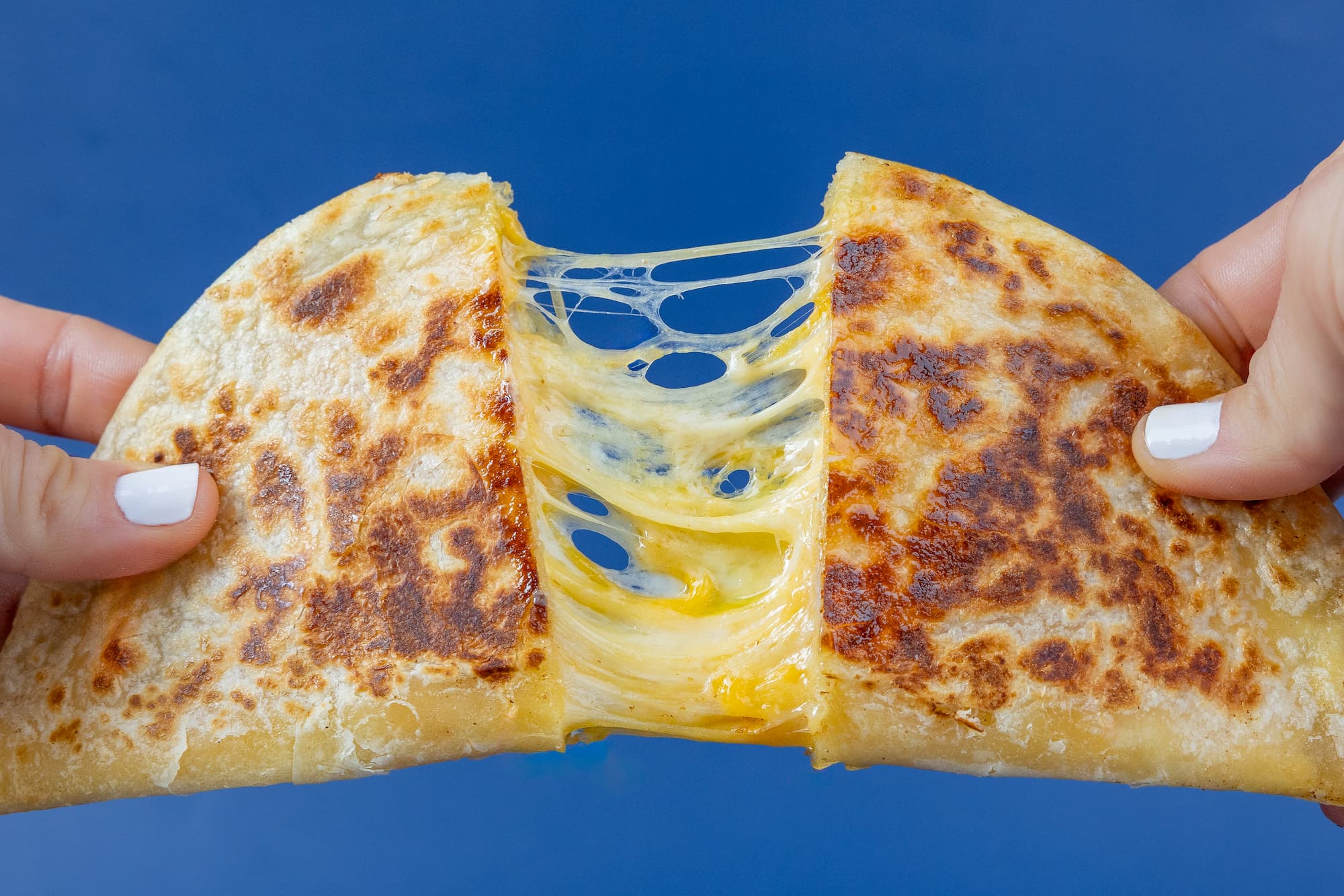 Ooey gooey chese quesadilla cut in half being pulled apart showing the cheese