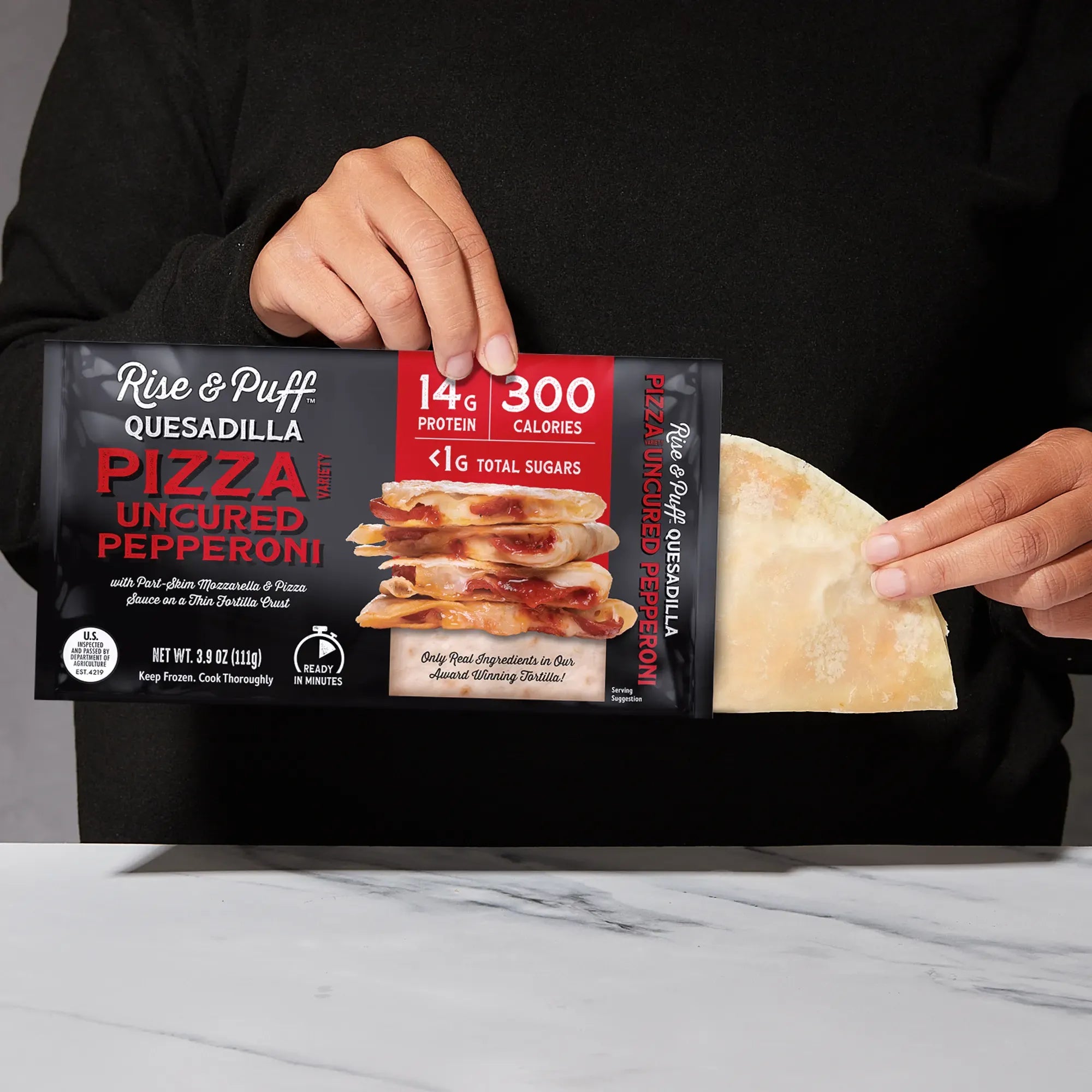 Rise & Puff Pizza Uncured Pepperoni Quesadilla shown coming out of its frozen retail packaging