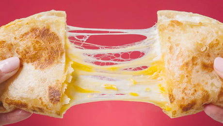 Cheese toastie being pulled apart with stretchy cheese on a red background