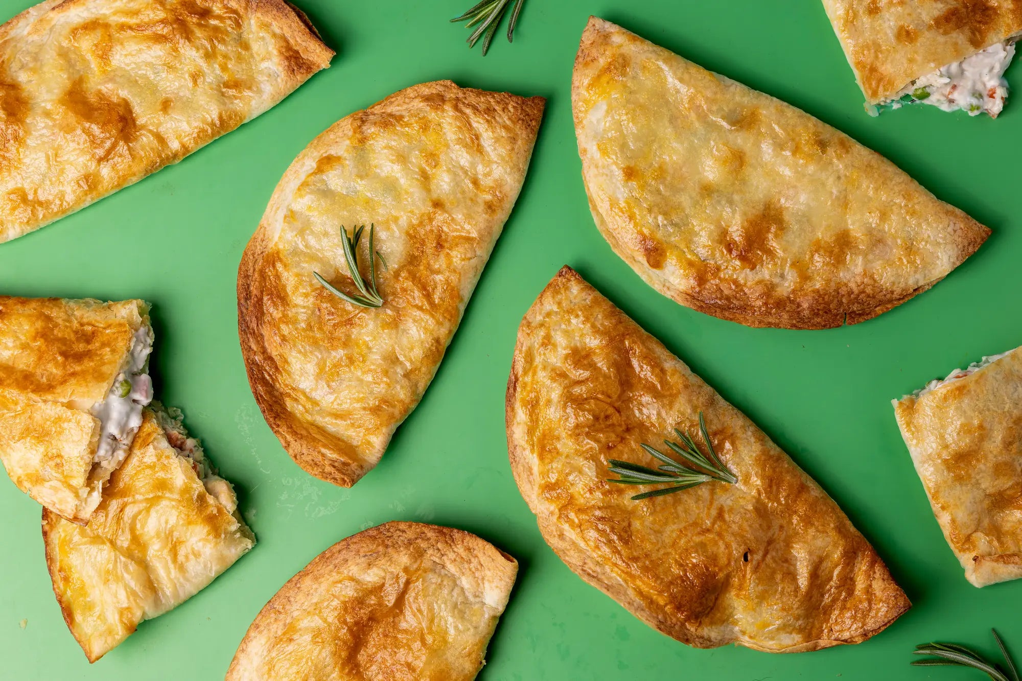 Birds-eye flat lay of golden flaky-crust Rise & Puff pot pies with fresh rosemary on a green background
