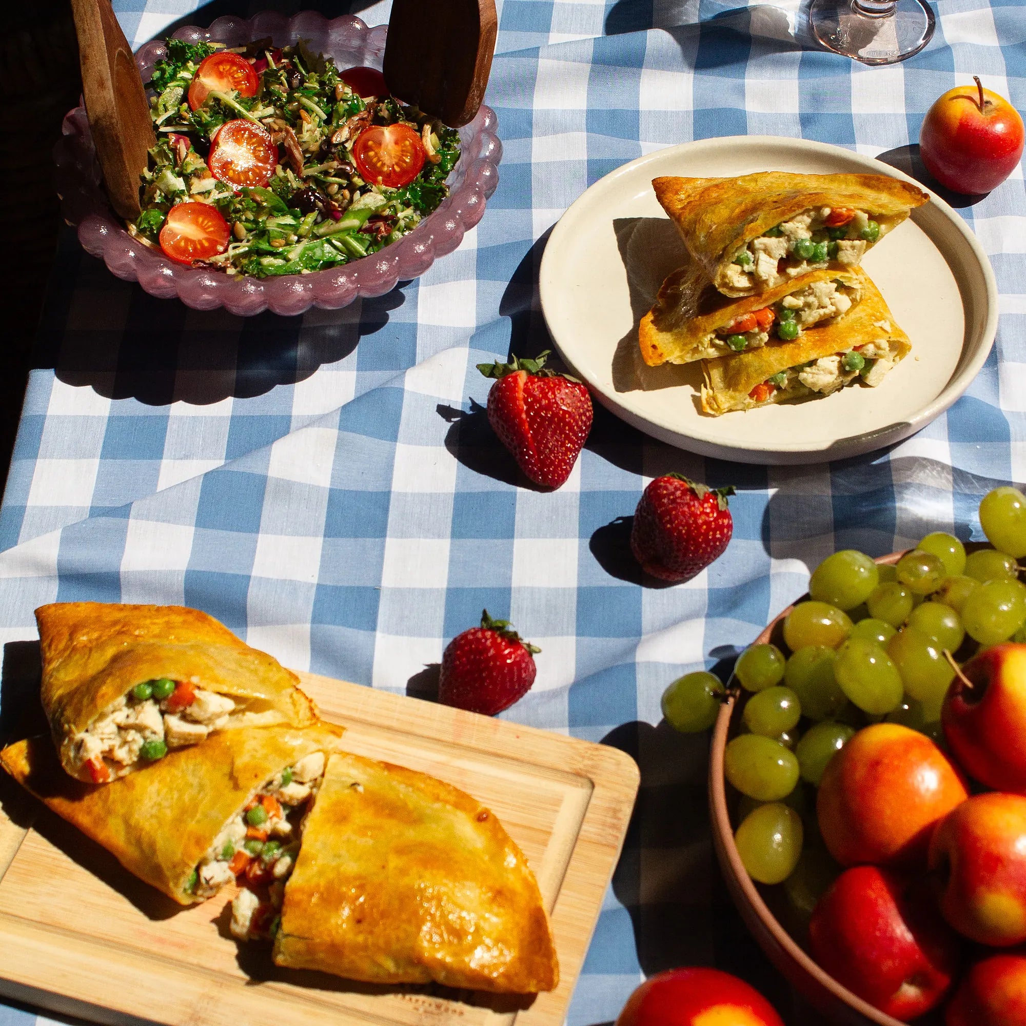 Rise & Puff Thin Crust Chicken Pot Pie served at an outdoor picnic table with salad, strawberries and grapes on a blue gingham cloth