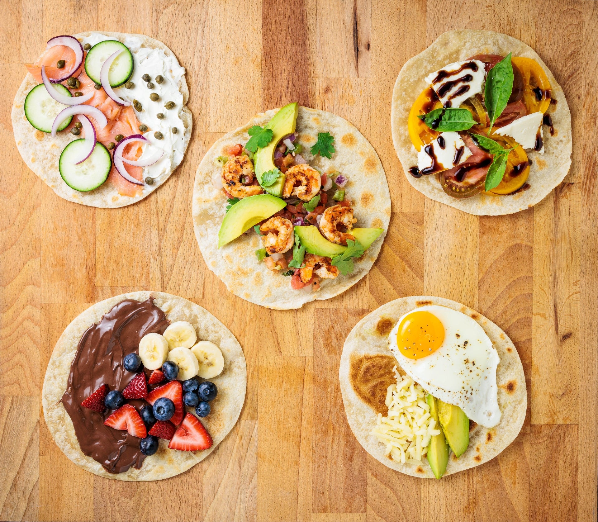 Five tortillas with various toppings on a wooden surface