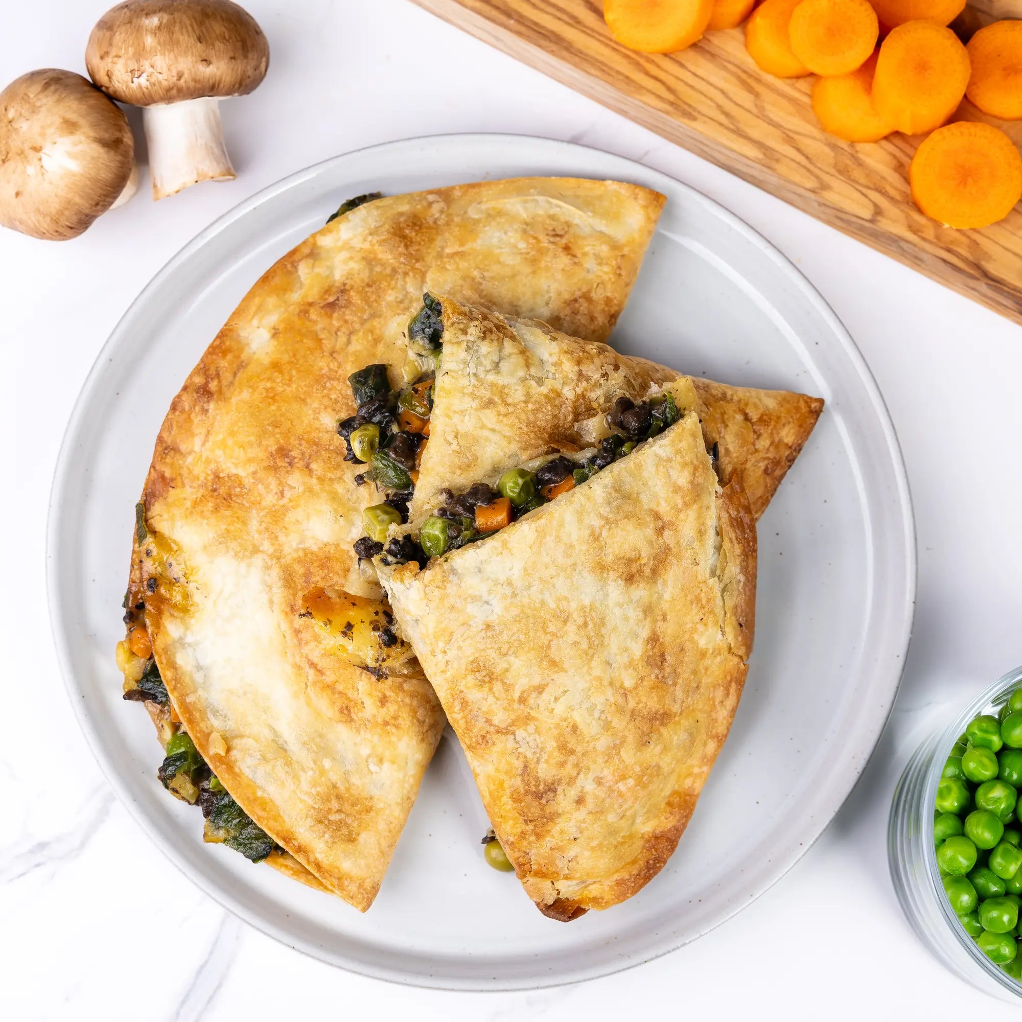 Close-up of Rise & Puff Vegetable Pot Pie cut open on a plate, showing peas, carrots, and spinach filling with fresh mushrooms and vegetables